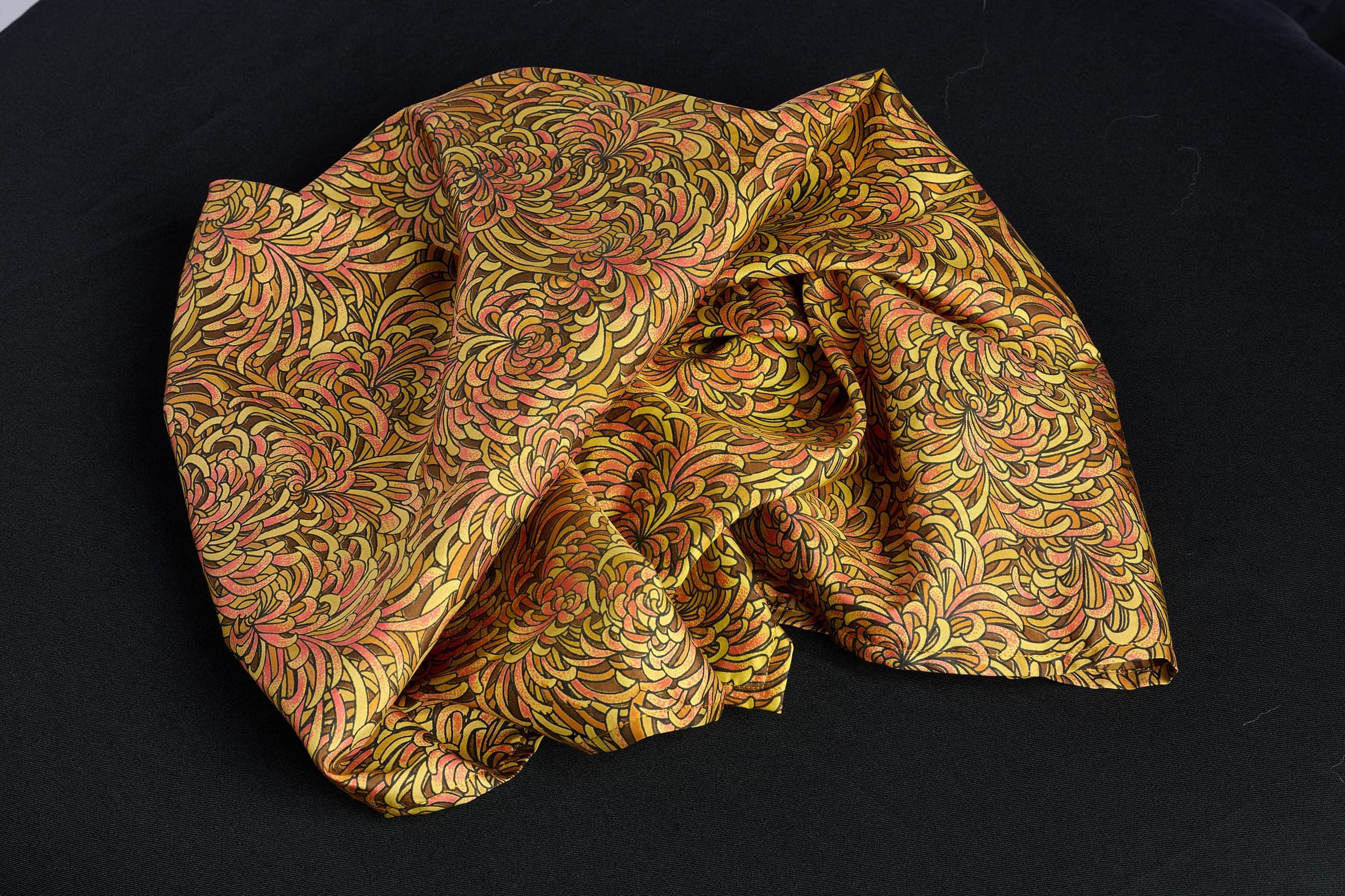 The Chrysanthemum silk scarf laid flat, showing the full amber and coral print
